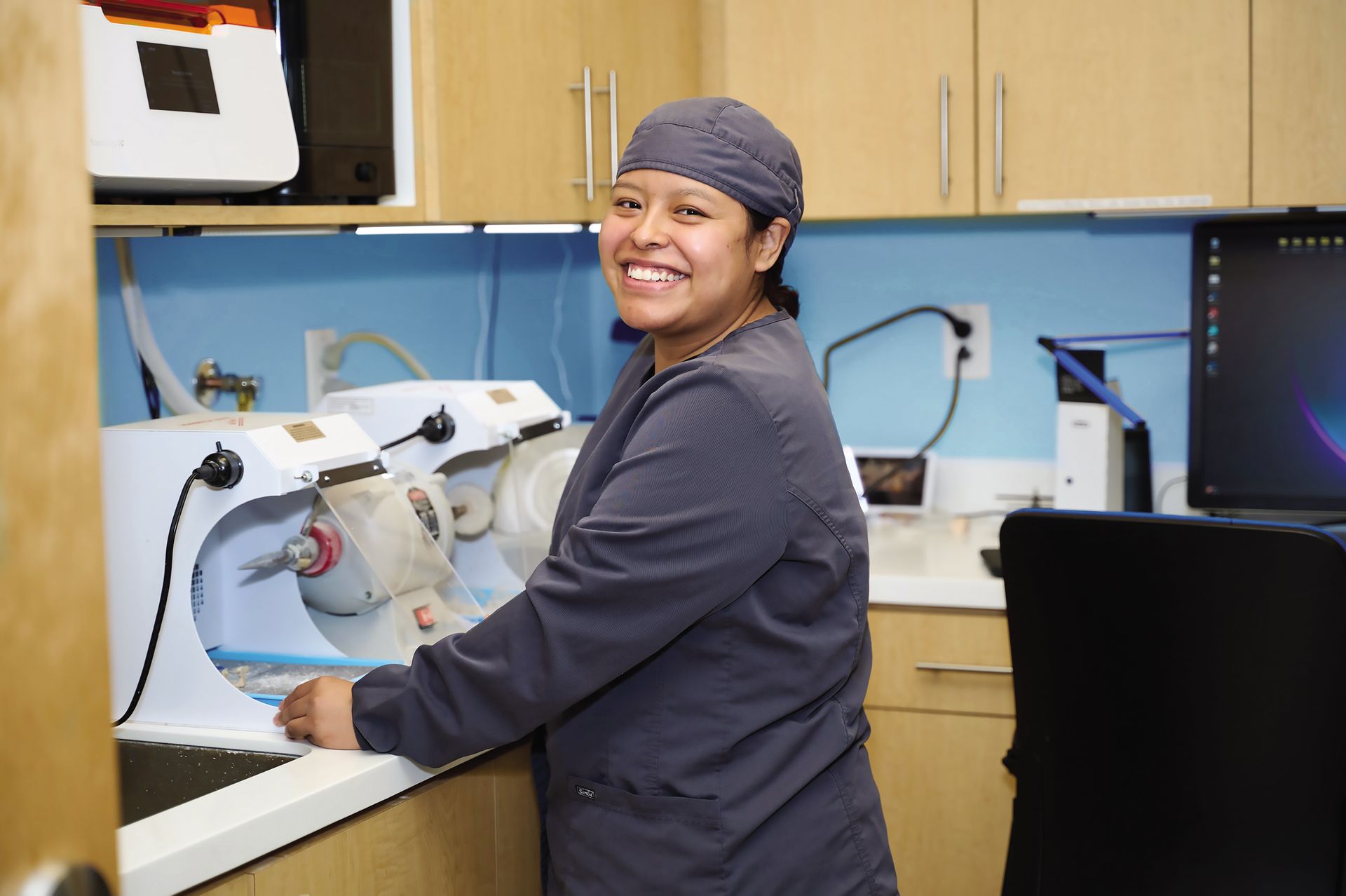 Person smiling in a lab coat at a workbench with equipment in a laboratory setting
