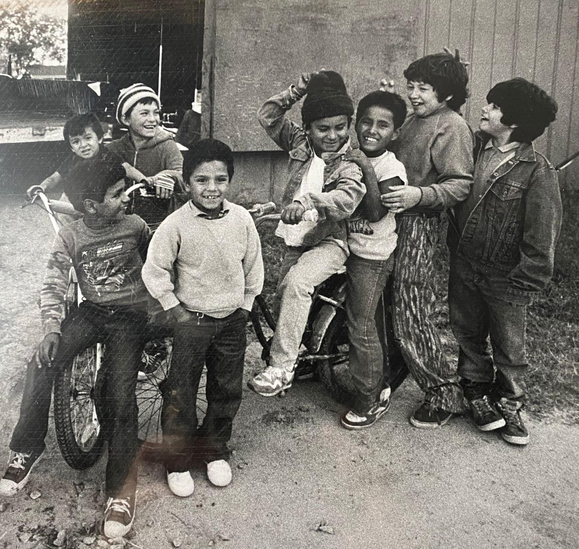 A group of children pose outdoors beside a bicycle, smiling and clustered together.