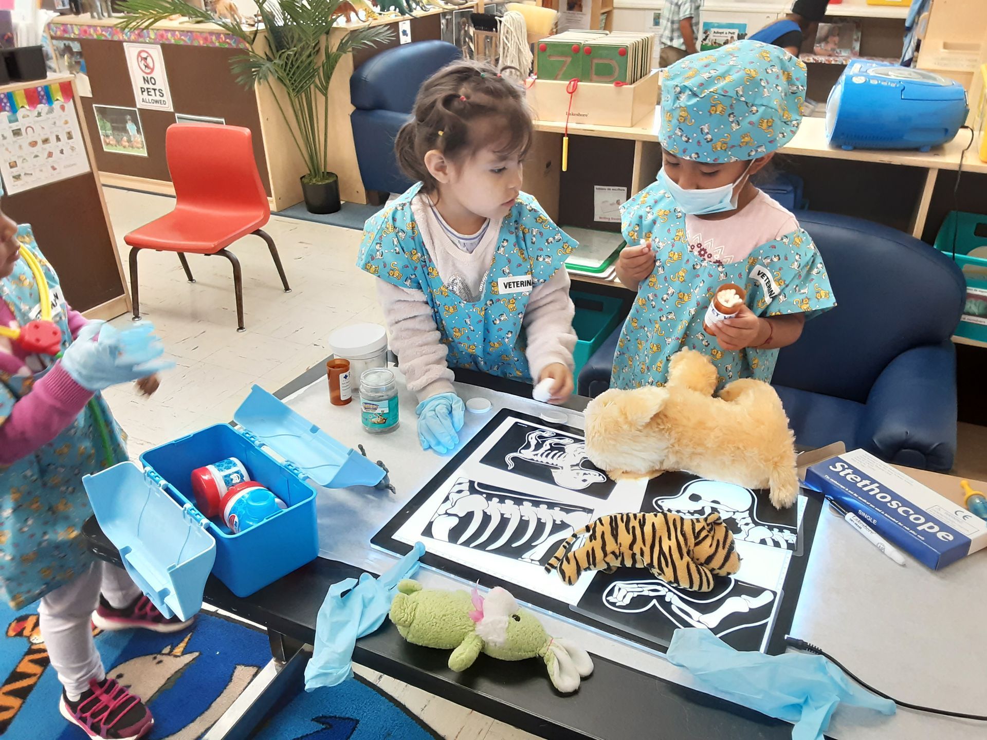Two children playing with plush animals at a table in a classroom or play area