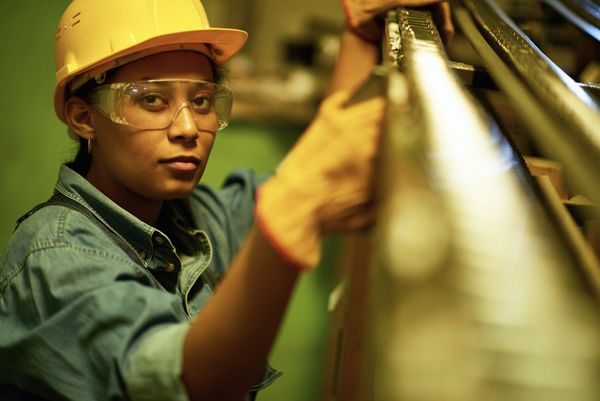 Worker in yellow hard hat and safety glasses inspecting equipment in an industrial setting