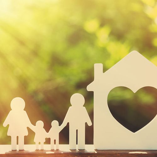 Family silhouettes beside a house cutout with a heart window on a warm, blurred background