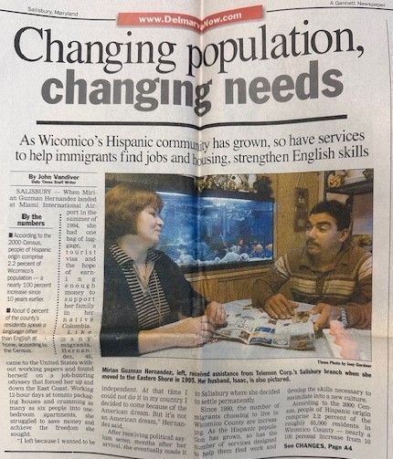 Newspaper article titled “Changing population, changing needs” with photo of two people talking at a table and aquarium behind them