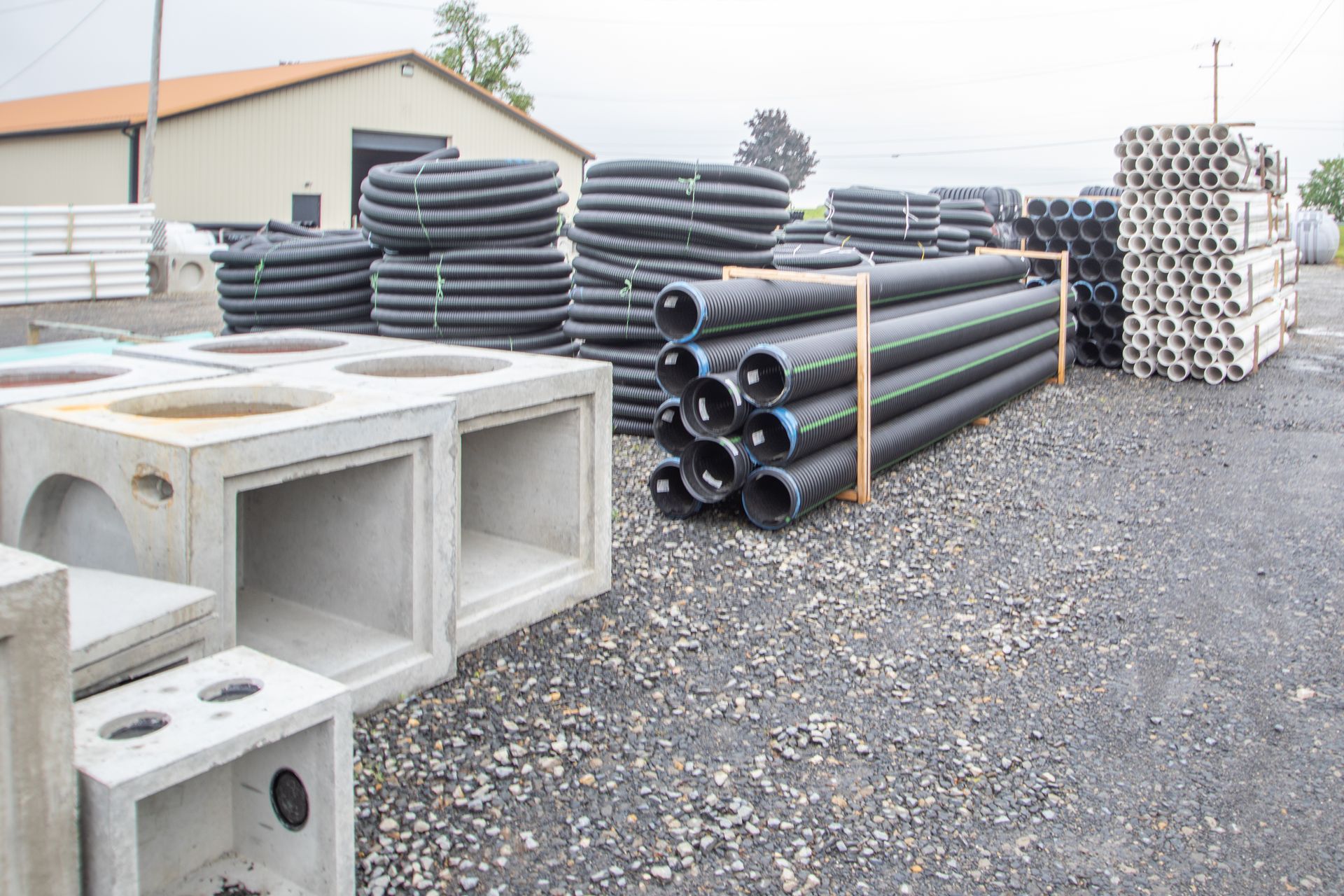 Concrete drainage structures and black plastic pipes stacked outdoors.