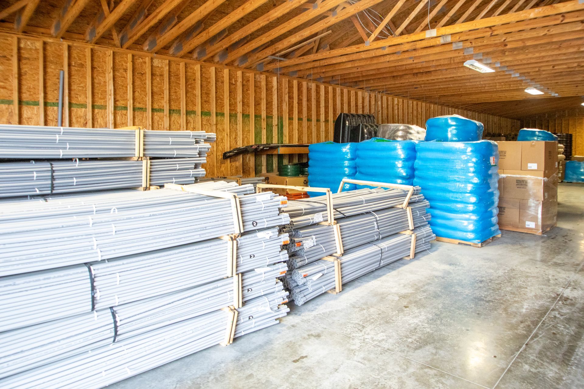 Warehouse interior with stacks of gray and blue plumbing supplies. Wooden beams and walls.