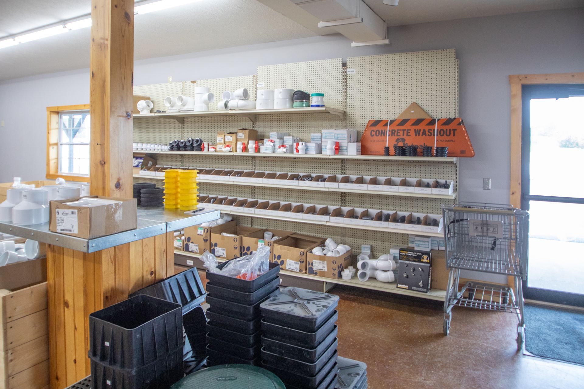 Interior of a shop with shelves of supplies; boxes and containers on the floor; a door and a window.