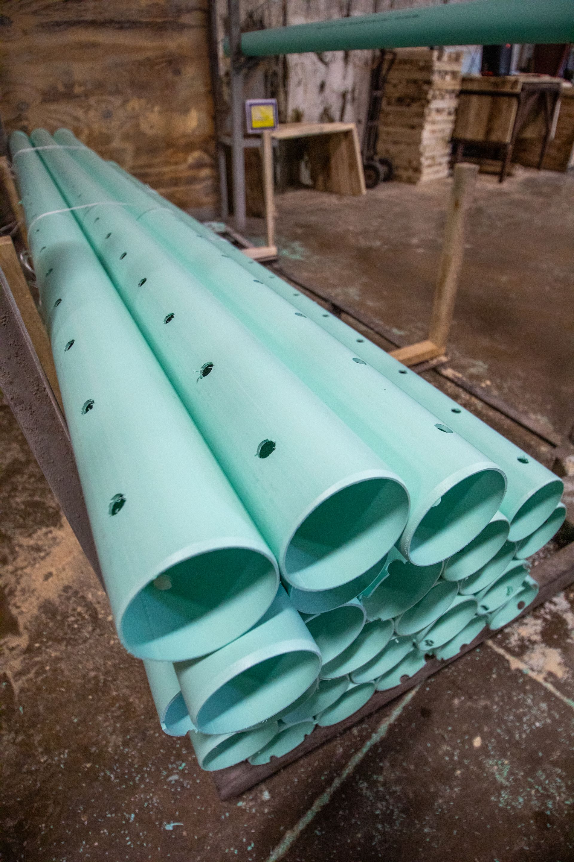 Stack of light green, perforated PVC pipes, possibly for construction, on a wooden surface.