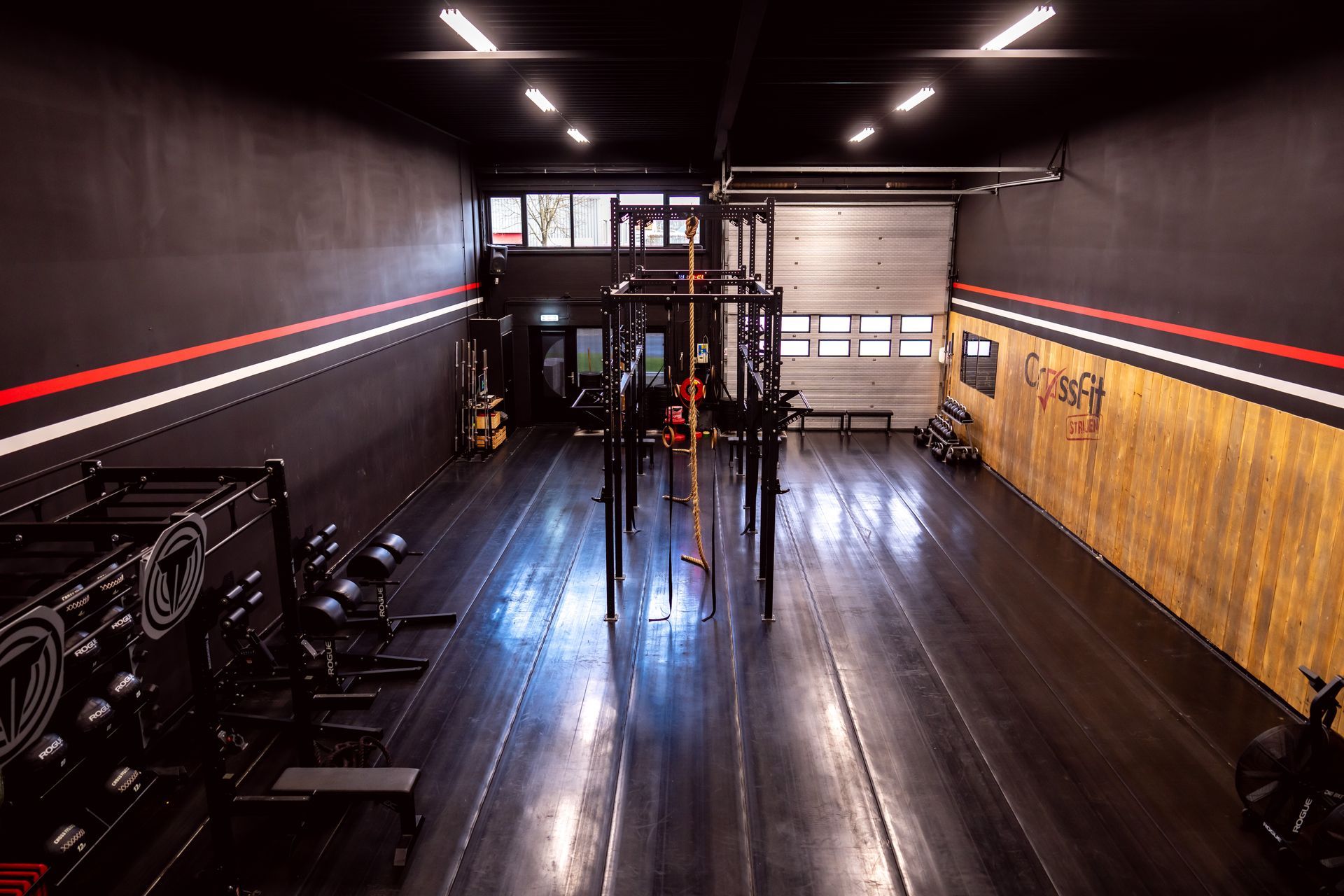 Een grote fitnessruimte met veel apparatuur en een garagedeur.