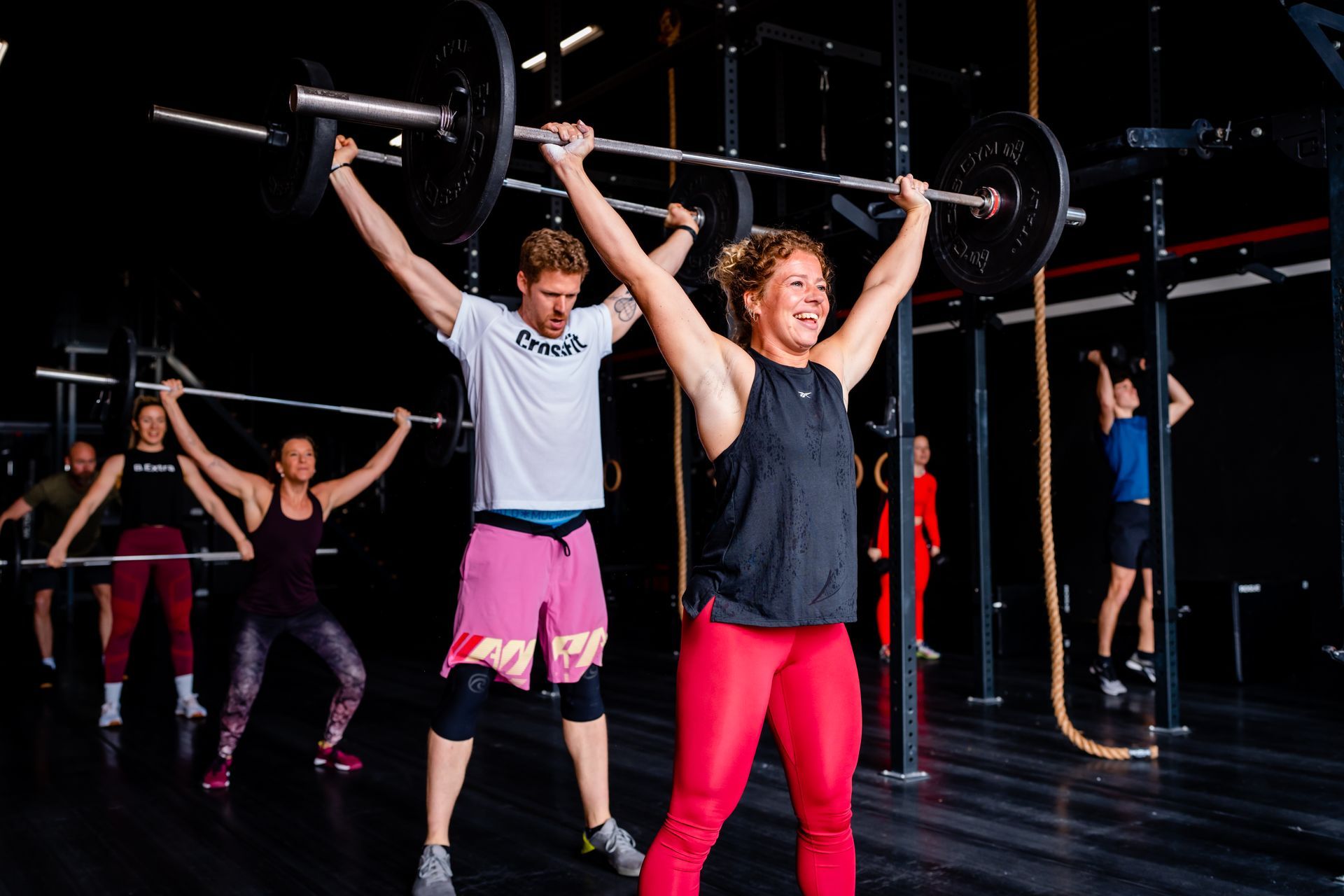 Een man en een vrouw tillen een halter boven hun hoofd in een sportschool.