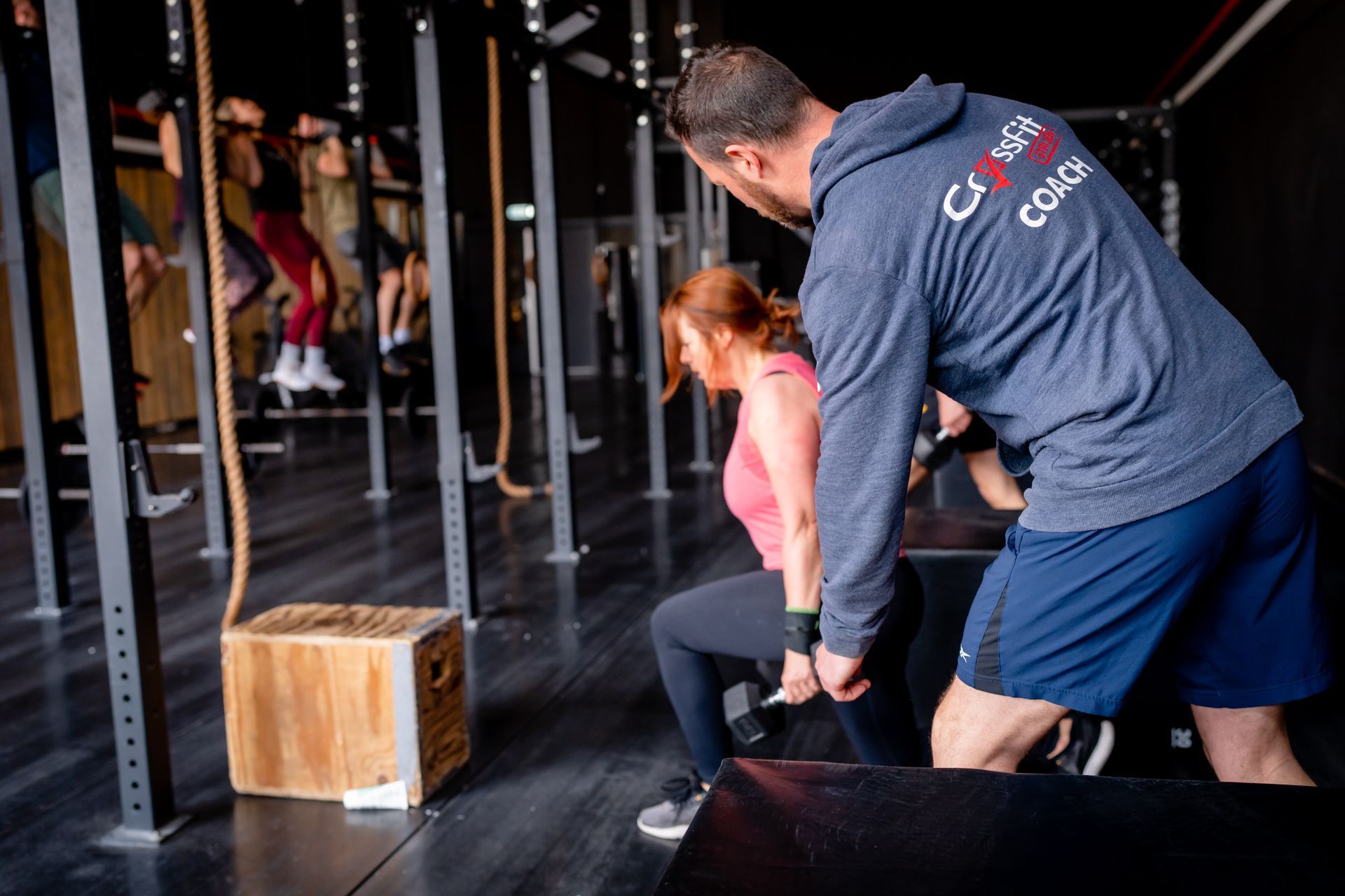 Een man in een crossfit-hoodie helpt een vrouw te hurken in een sportschool.