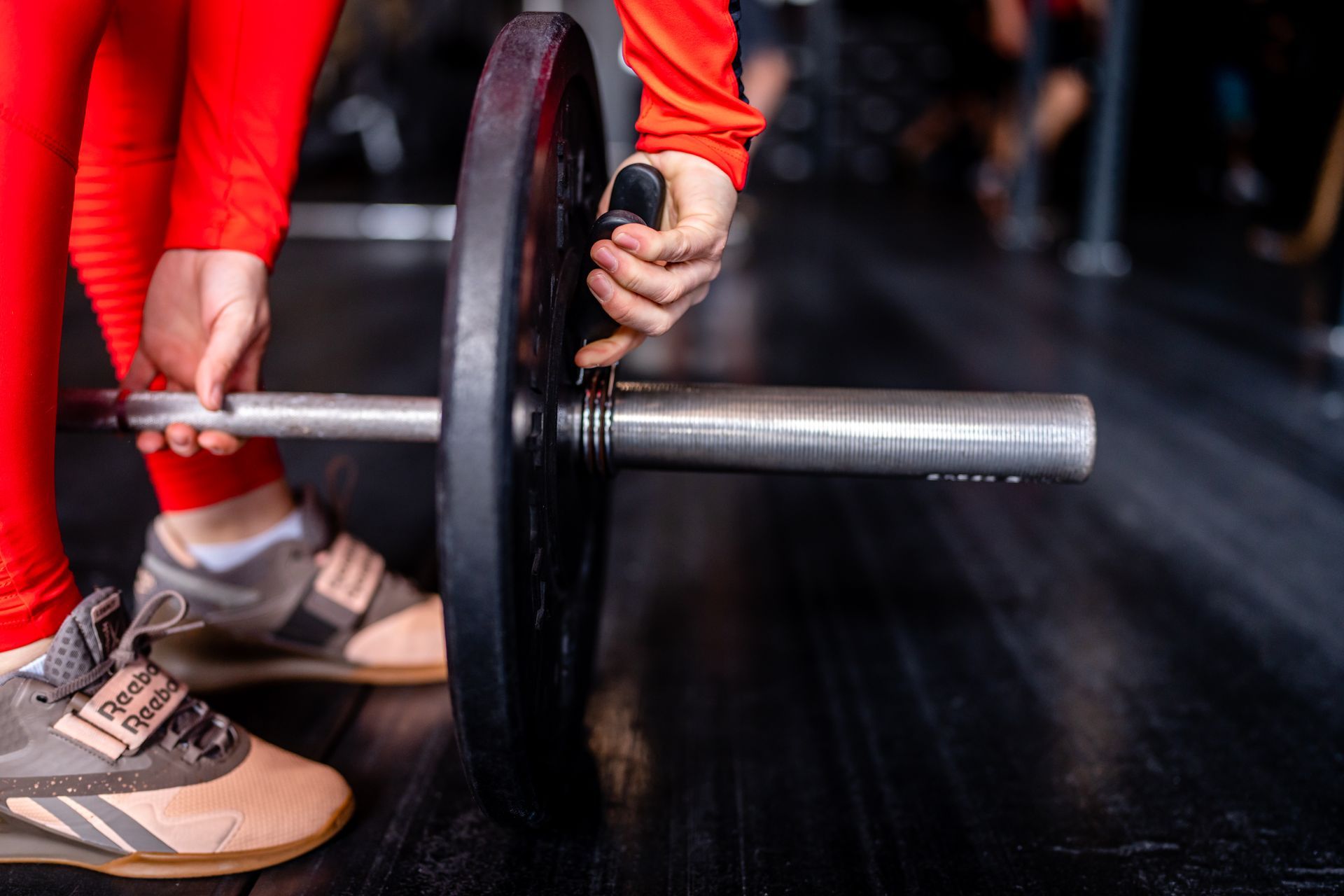 Persoon in rode kleding plaatst gewichtsschijven op een halterstang in een sportschool.