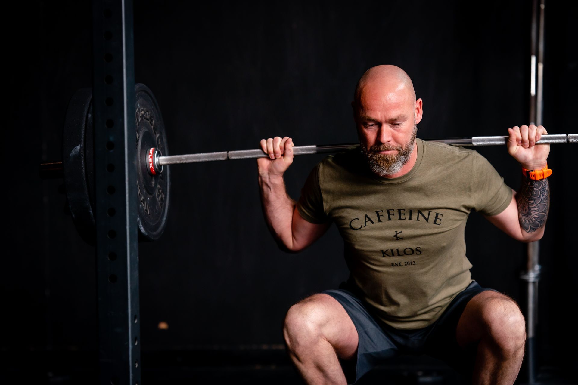 Een man doet squats met een halter in een sportschool. Hij draagt een groen shirt