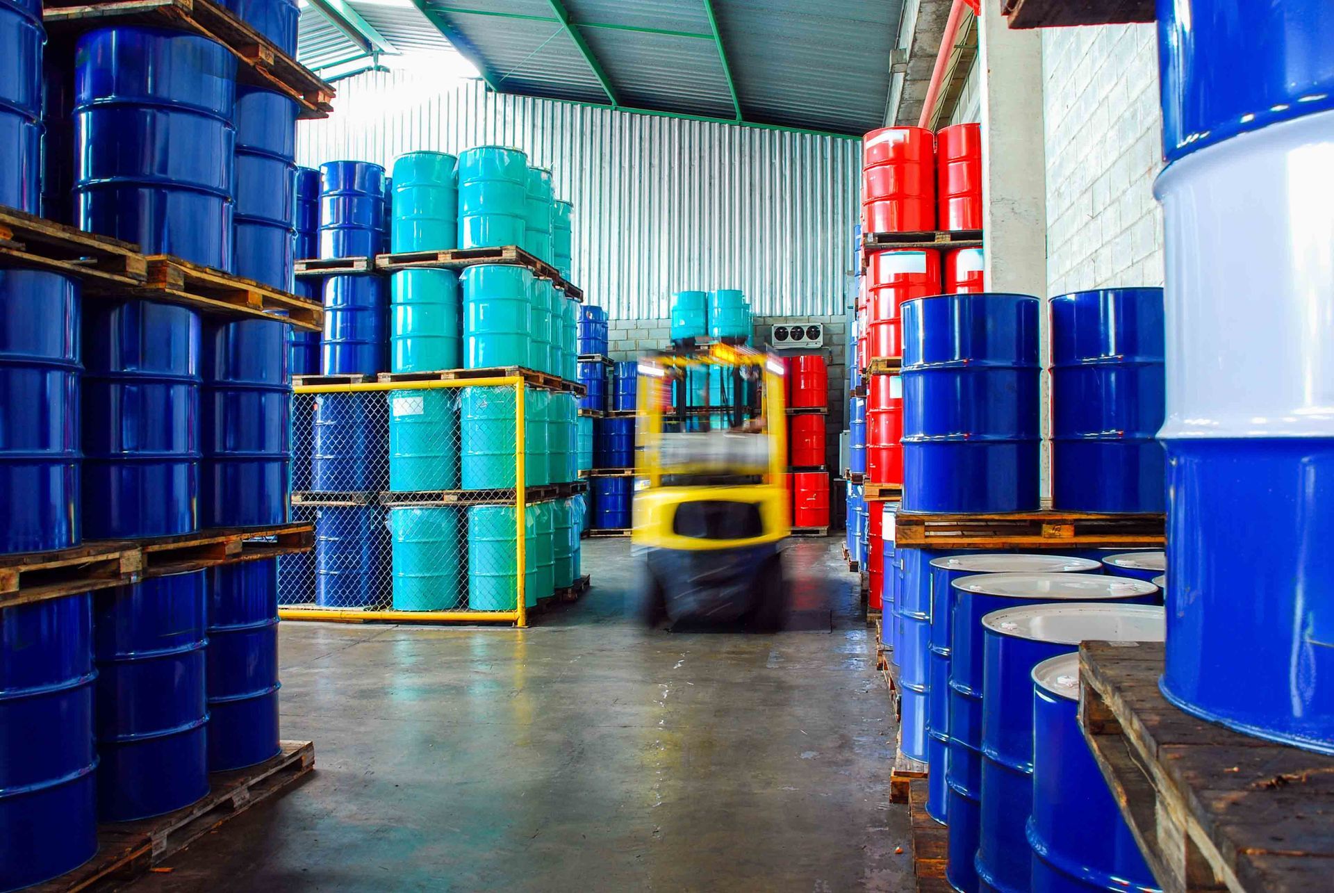 Warehouse aisle with stacked blue and red barrels and a forklift in the center