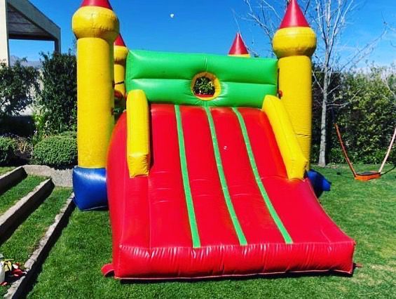 Casa inflable colorida con tobogán sobre césped verde.