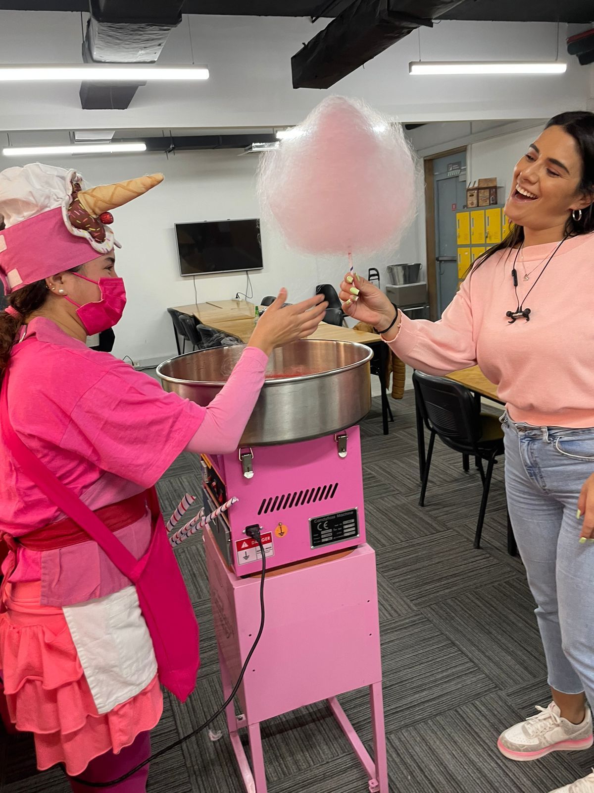 Fabricante de algodón de azúcar con traje rosa preparando golosinas para la gente en espacios interiores.