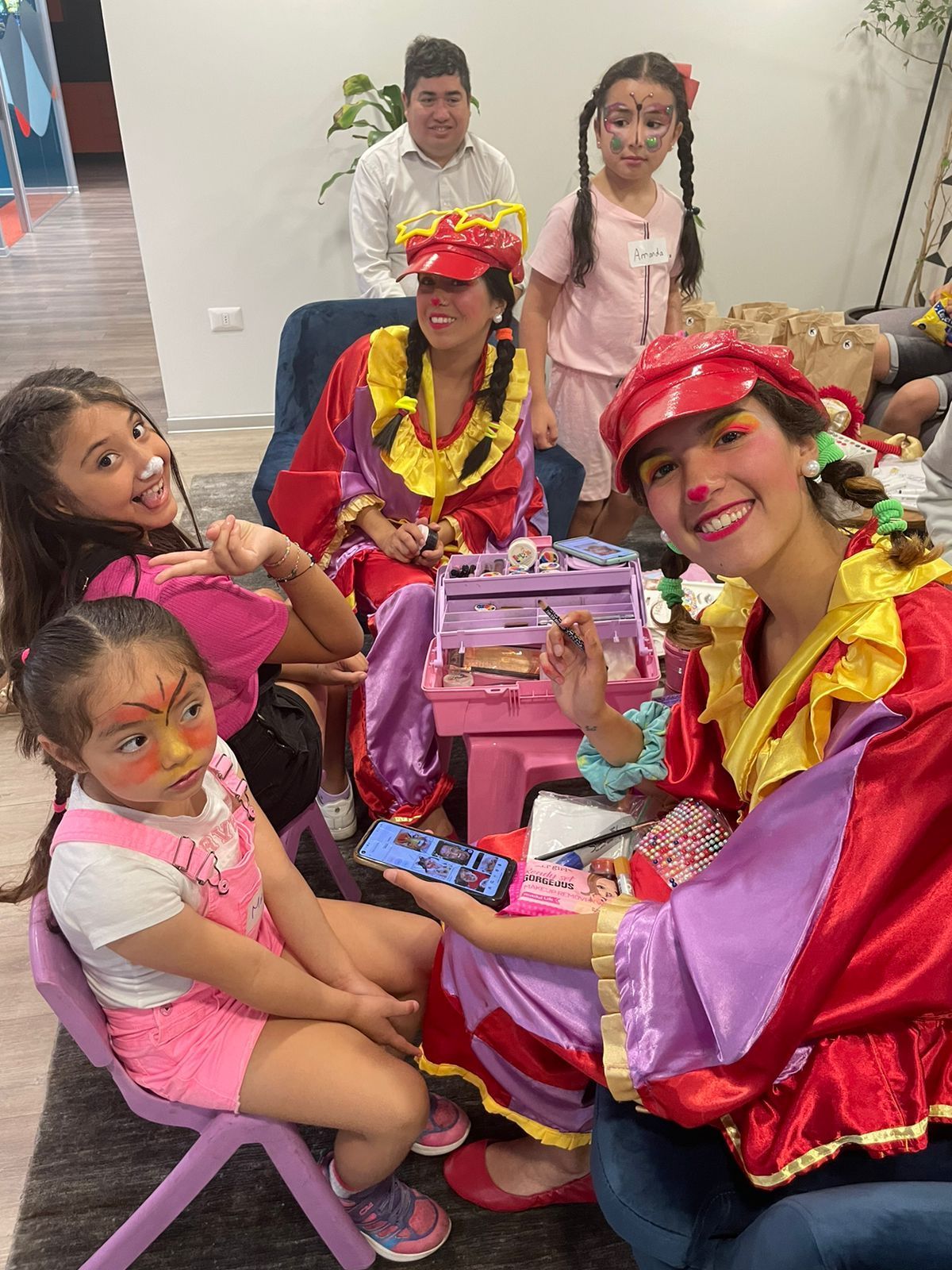 Payasos pintando caras en una fiesta. Niños sonriendo, fondo de arcoíris, texto 