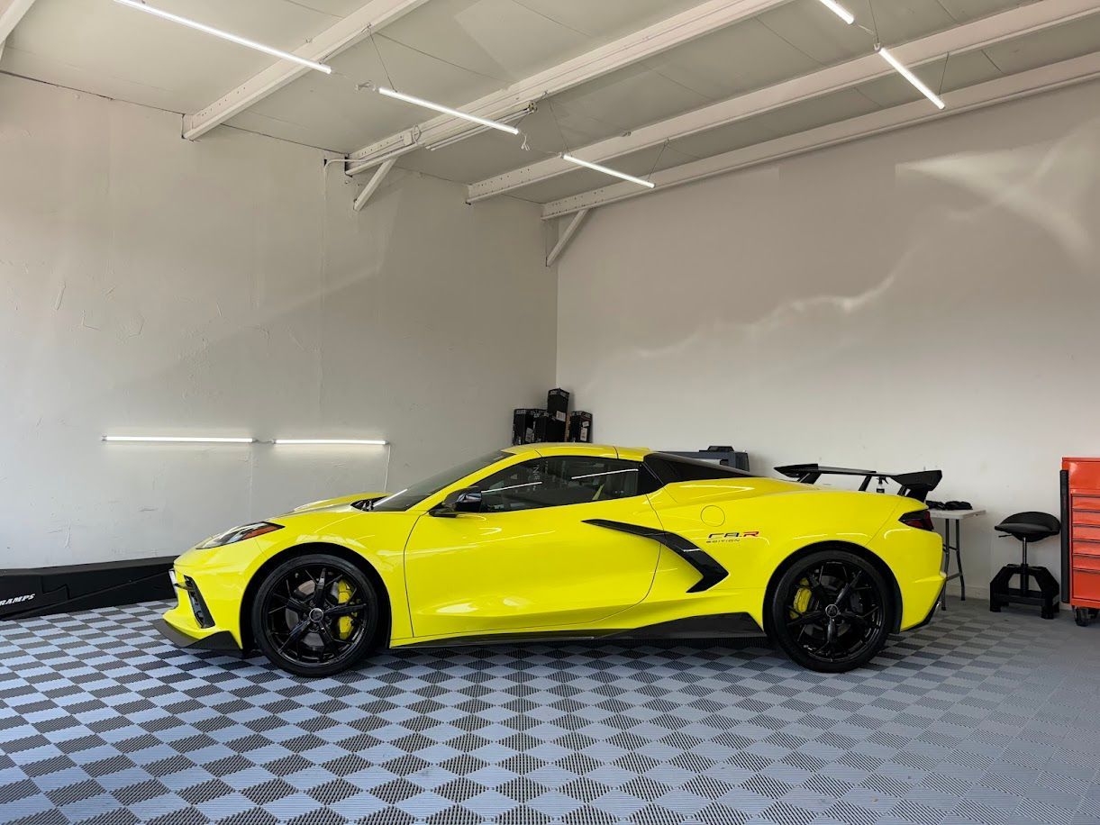 Yellow sports car in a garage with black rims, spoiler, and a checkered floor.