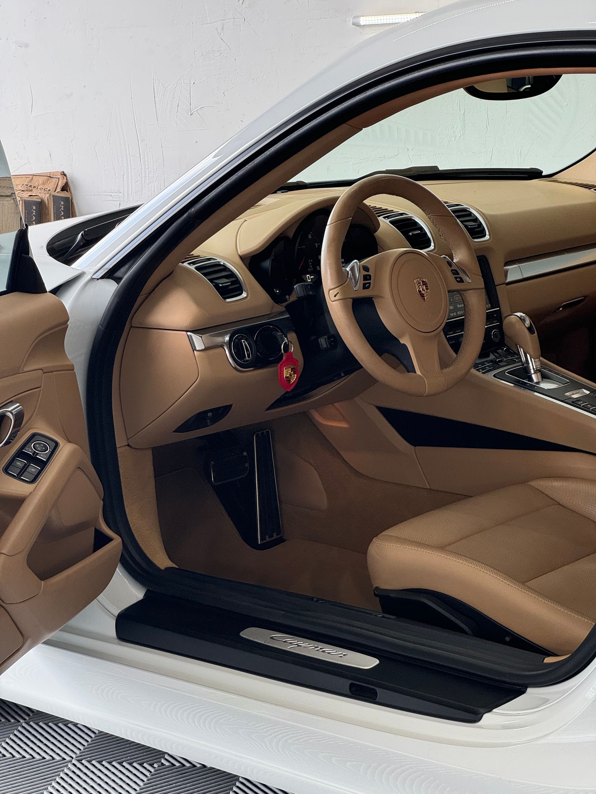 Interior of a white Porsche sports car with tan leather seats and steering wheel; door open.