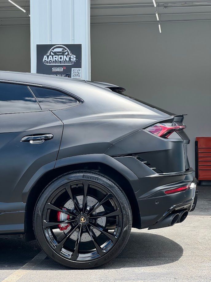 Black Lamborghini Urus SUV with black wheels and red brake calipers parked outside Aaron's shop.