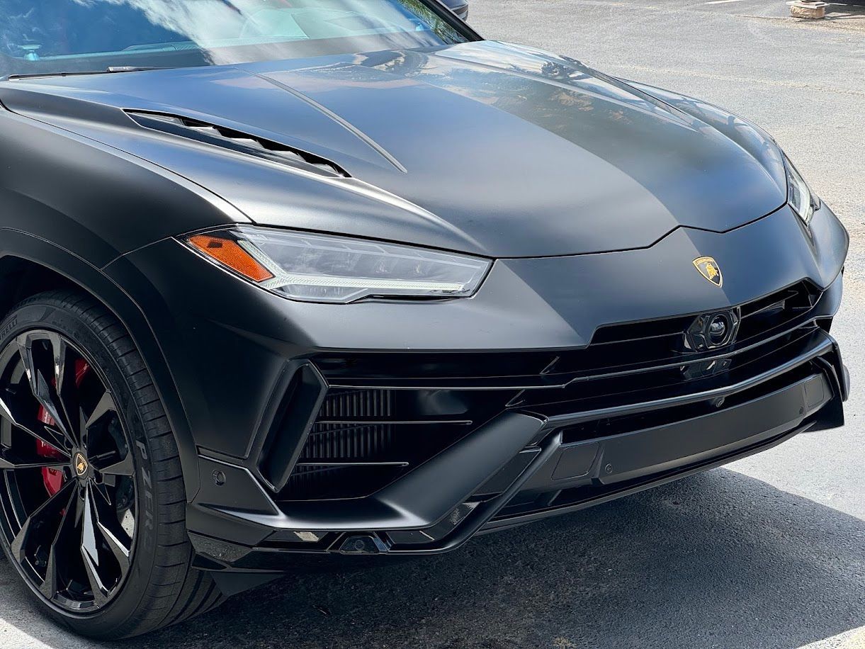 Black Lamborghini Urus SUV, front view. Matte finish, red brake calipers, daytime.