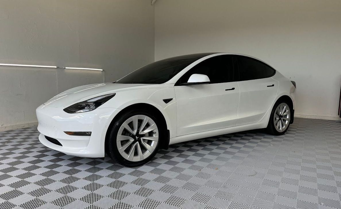 White Tesla Model 3 car parked in a garage with checkered flooring.