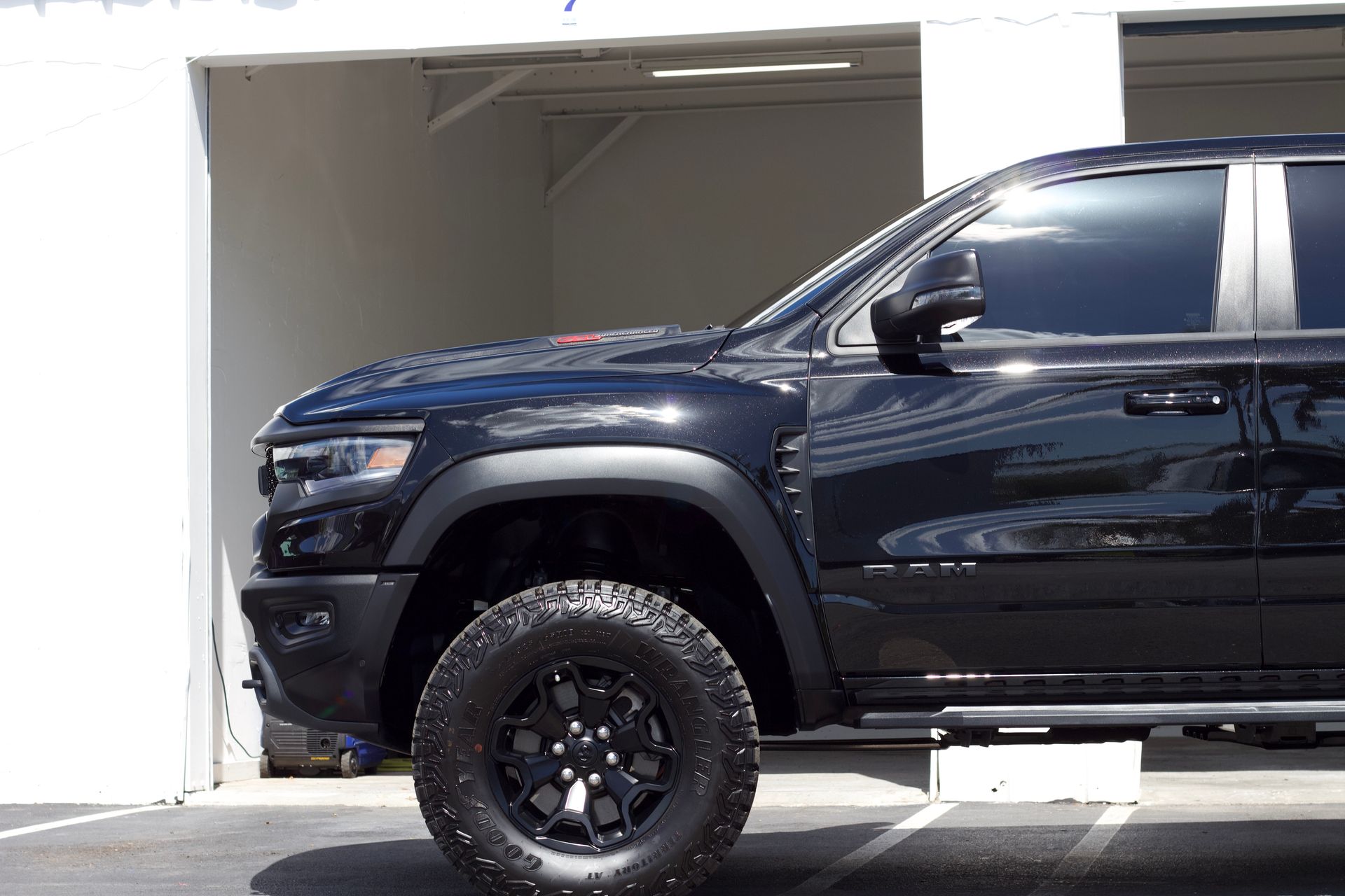 Black Ram truck with black wheels parked near a white building with an open garage.