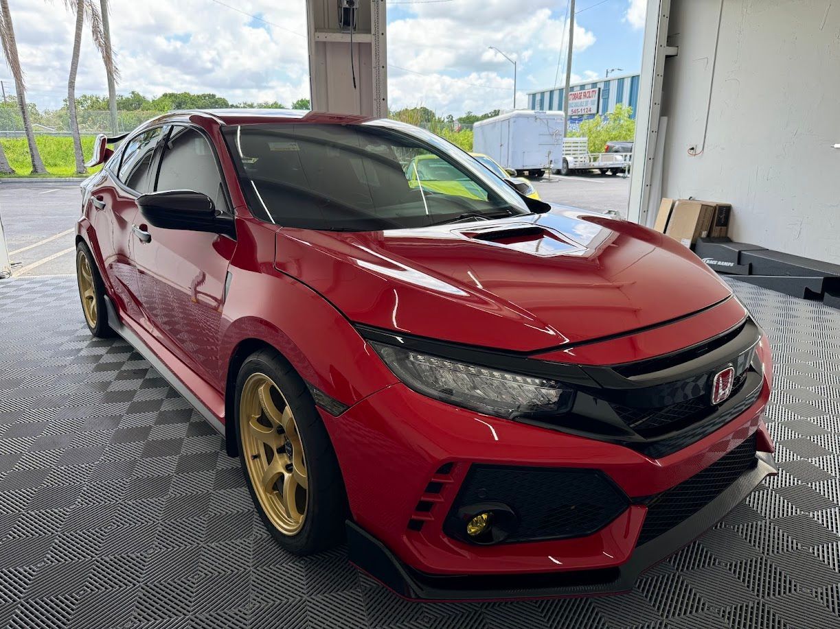Red Honda Civic Type R with gold rims parked indoors.