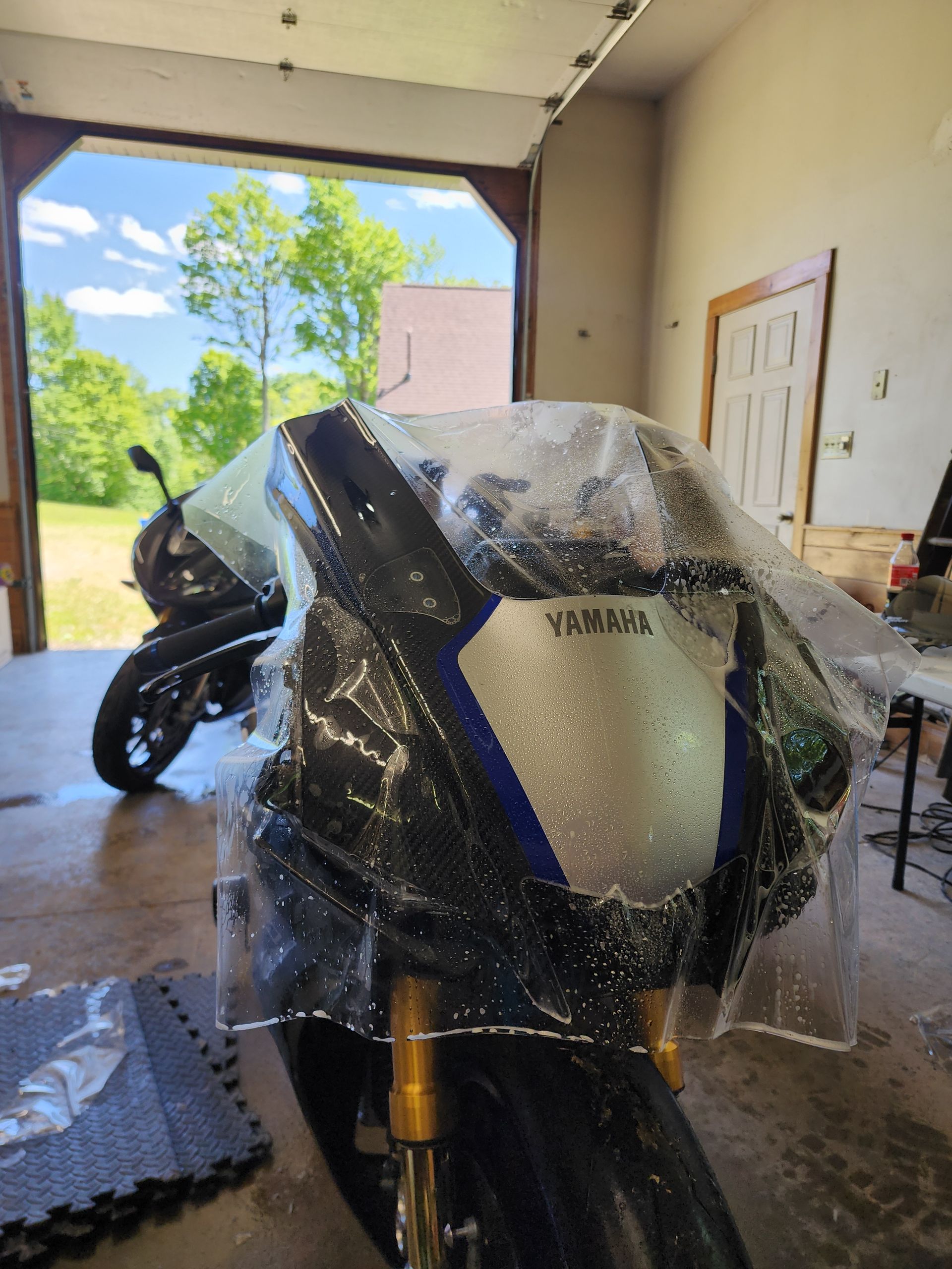 Yamaha motorcycle covered in plastic wrap inside a garage, another bike in background.