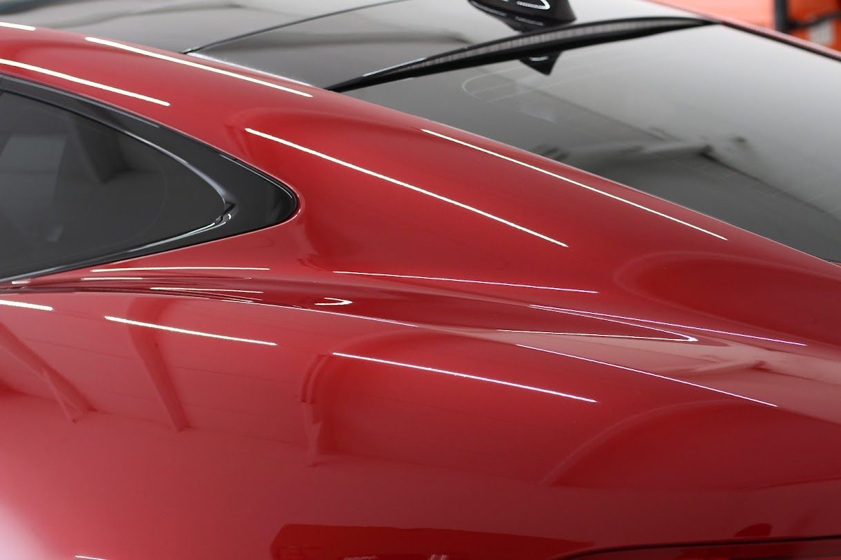 Red car's rear, glossy finish, reflecting bright lights; black trim, dark window visible.