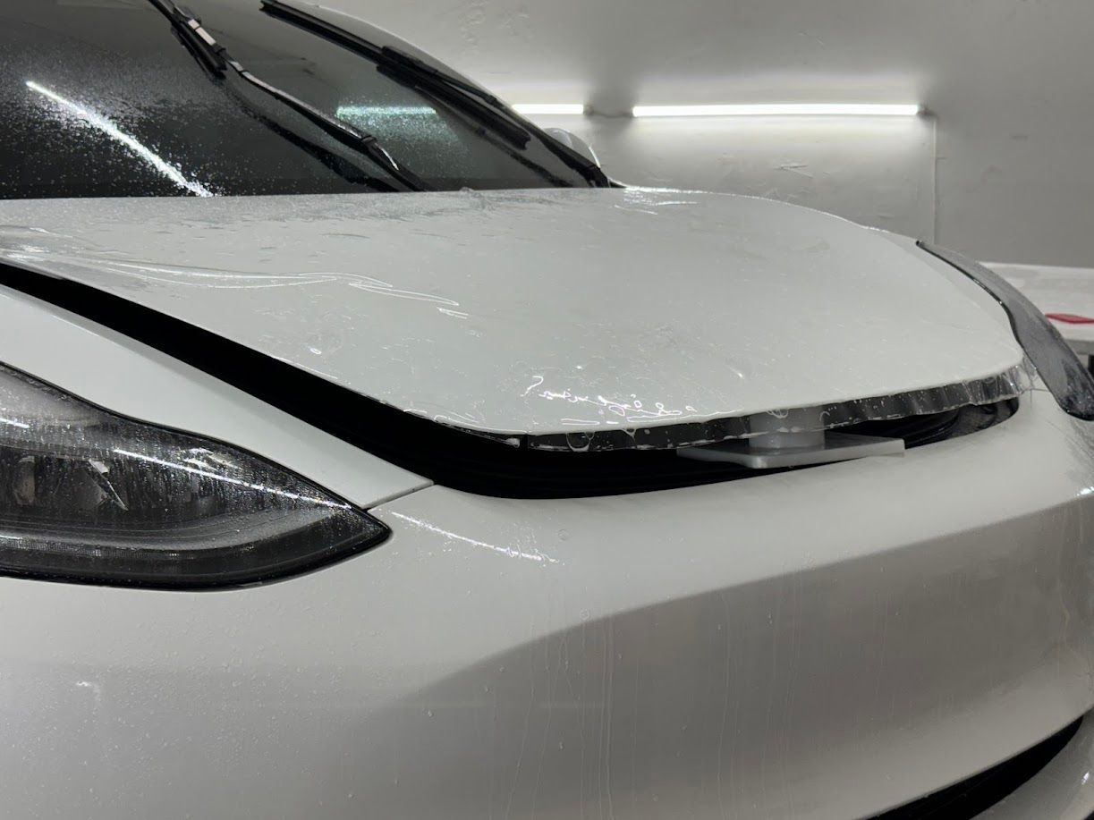 White car hood with clear film applied, in a bright workshop.