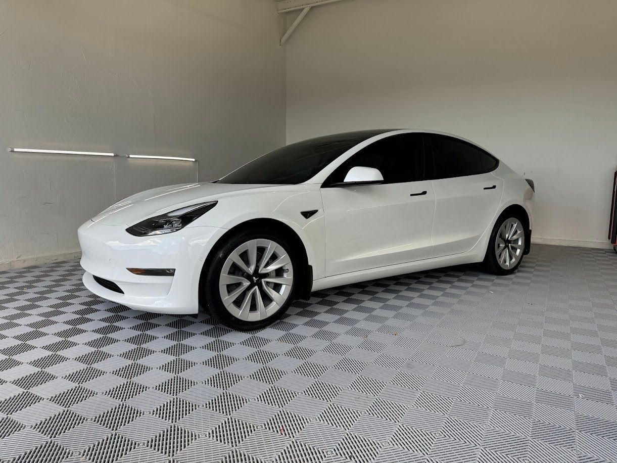 White Tesla Model 3 car parked on a checkered floor inside a garage.