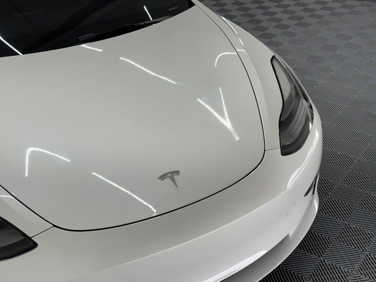 White Tesla car's front hood with the Tesla logo, indoors, angled shot.