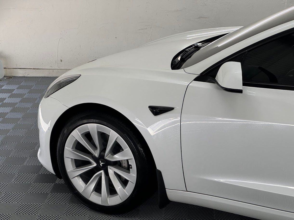 White Tesla car's front side, showing wheel, door, side mirror, and black side marker.