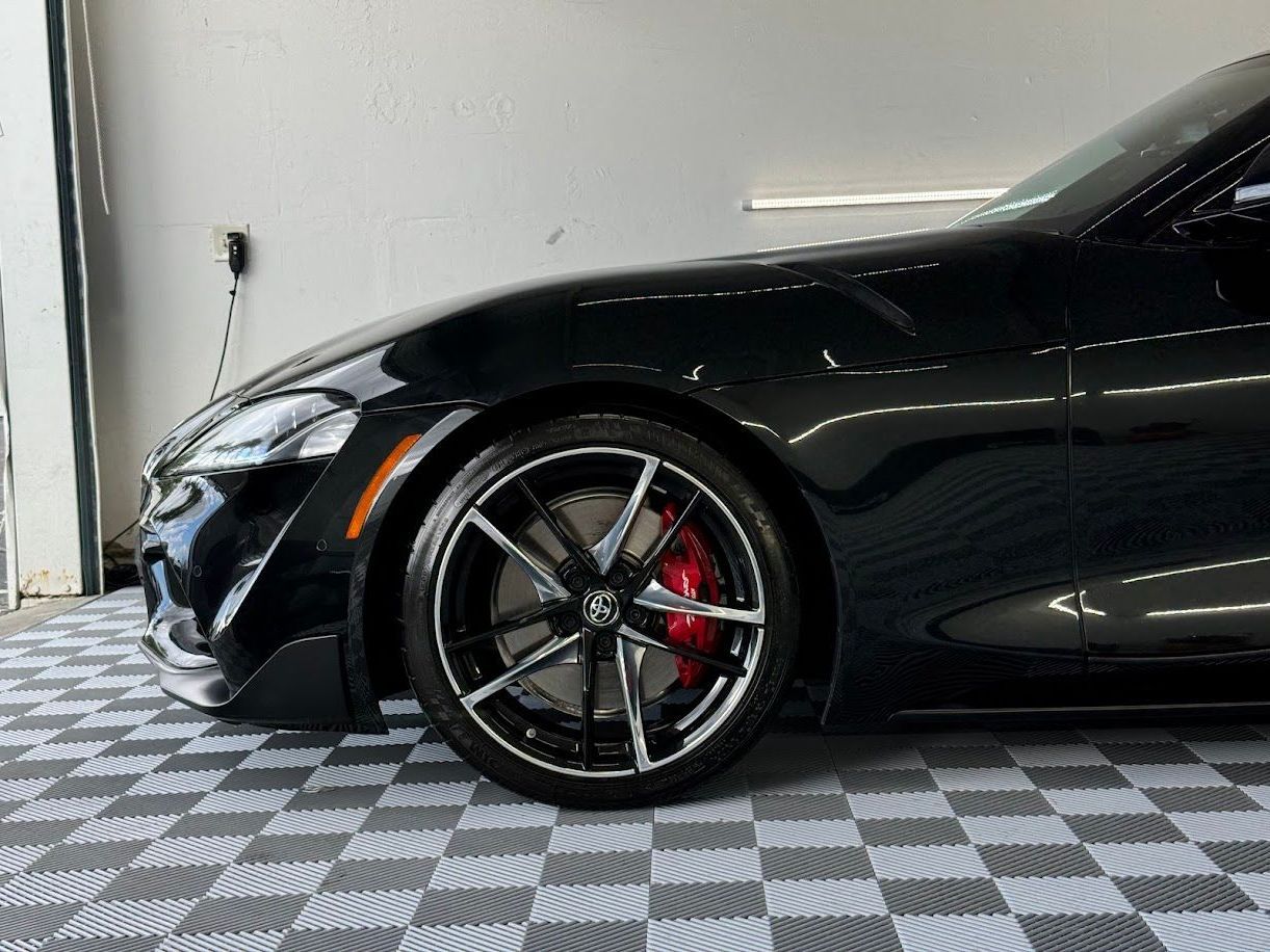 Black Toyota Supra sports car, front quarter view, black wheels, red brake calipers.