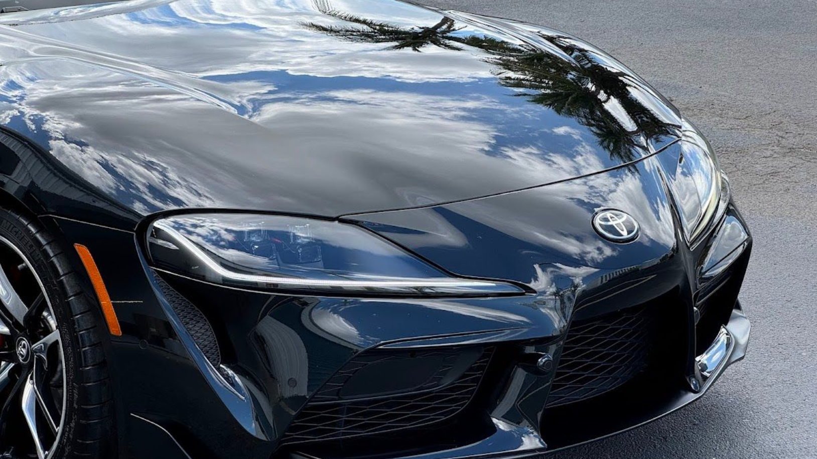 Black Toyota Supra car's front with reflective hood, displaying the sky.