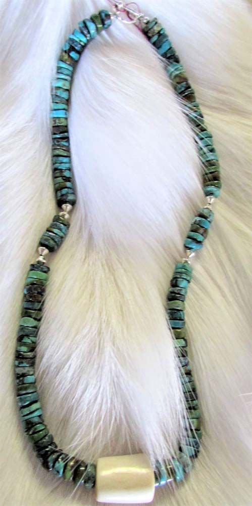 A necklace with turquoise beads and pearls is sitting on a white fur.