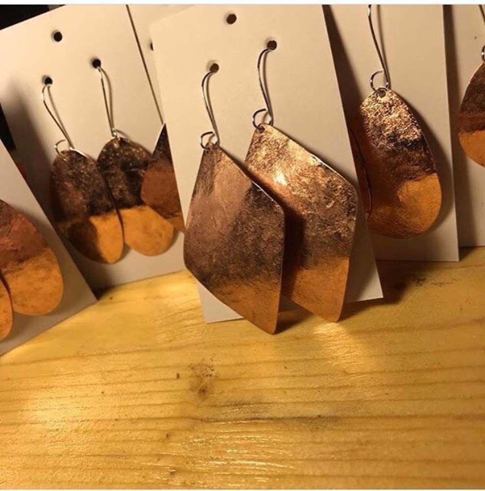 A group of copper earrings are sitting on a wooden table