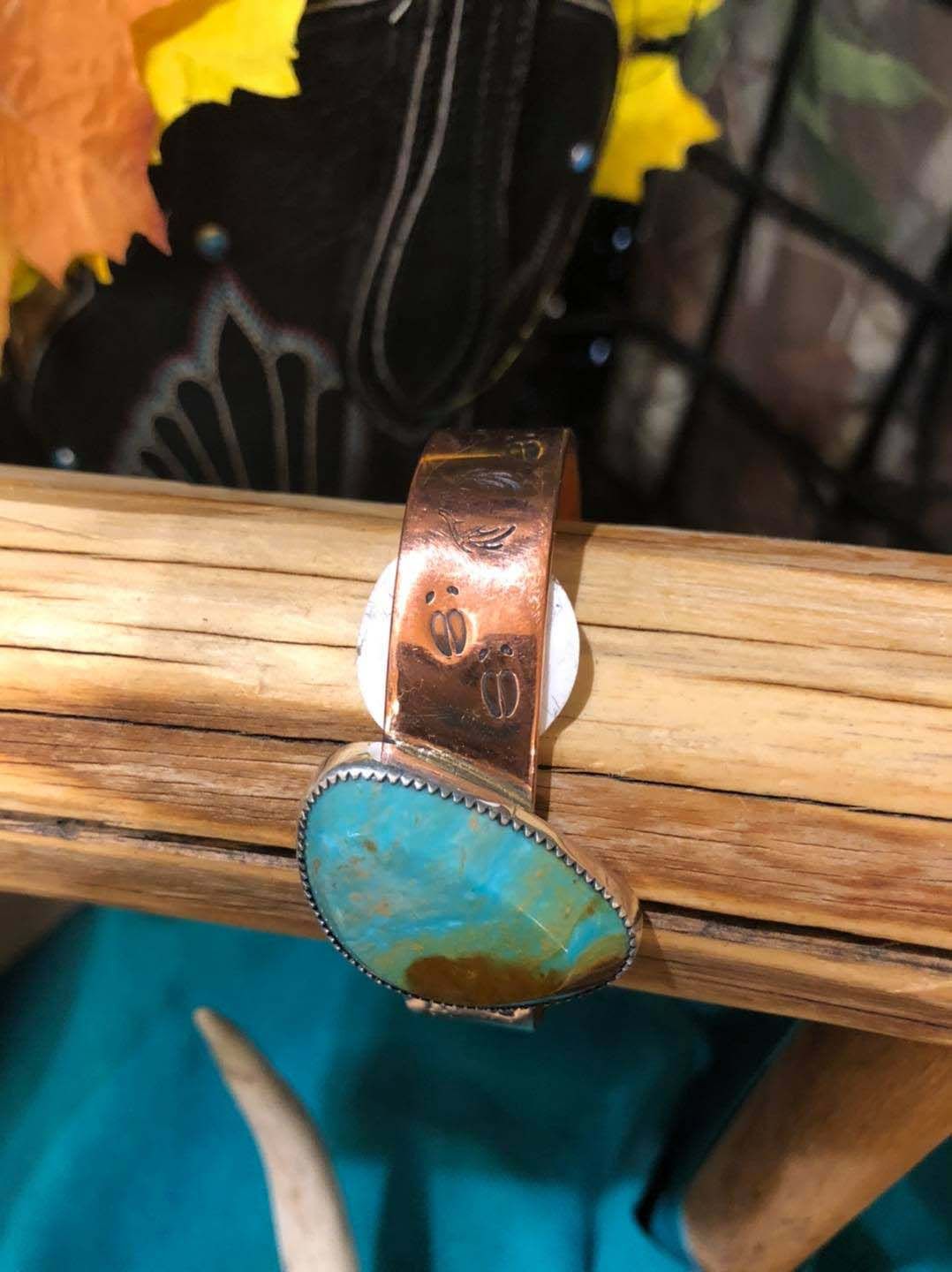 A copper ring with a turquoise stone is sitting on a wooden table.
