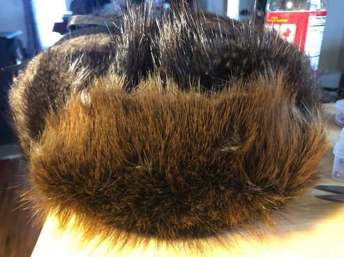 A person is holding a fur hat on their head.