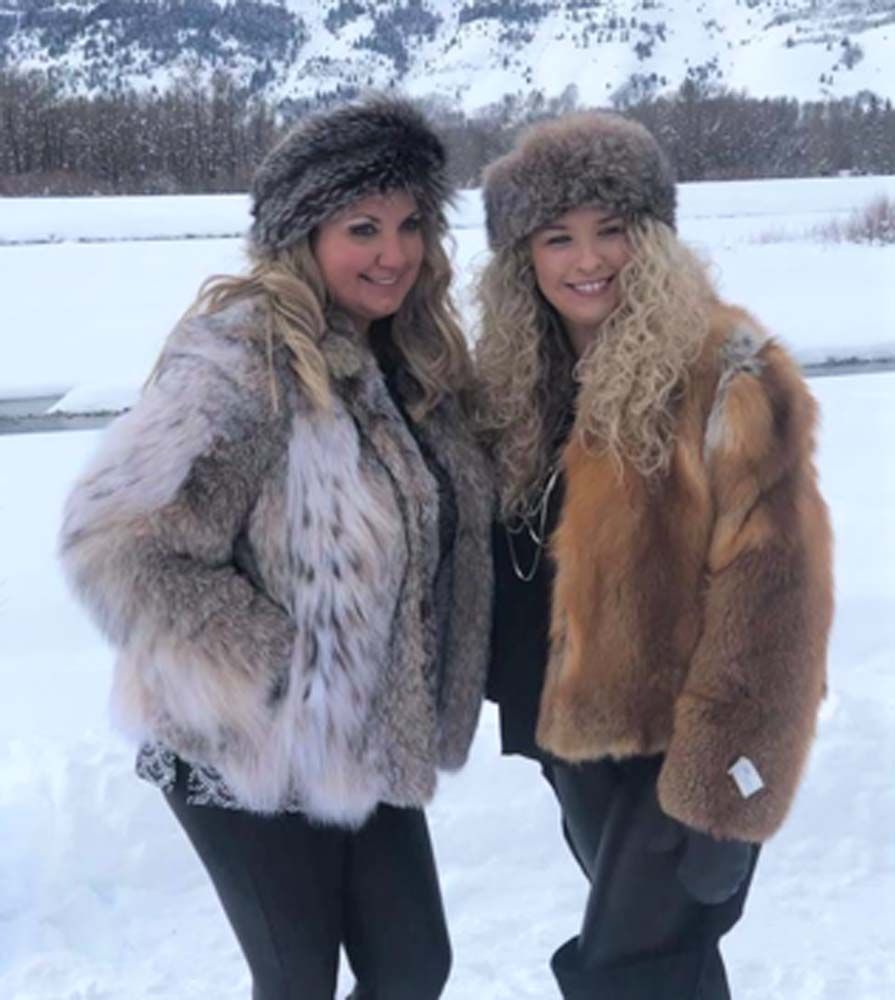 Two women standing in the snow wearing fur coats and hats