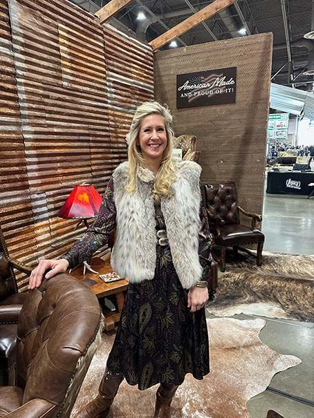 A woman in a fur vest is standing in front of a chair.