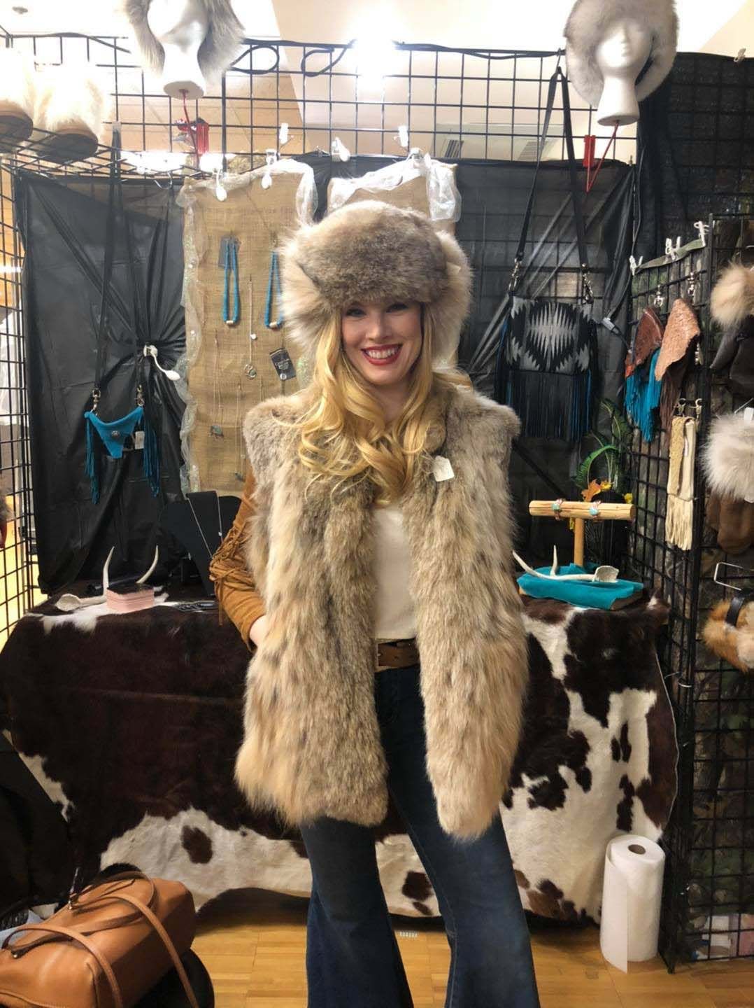 A woman wearing a fur vest and hat is standing in a store.