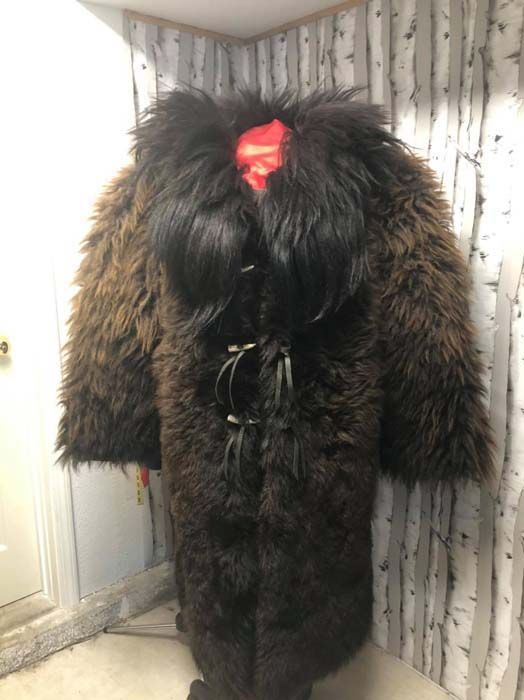 A brown fur coat with a red bow on the back is standing in a room.