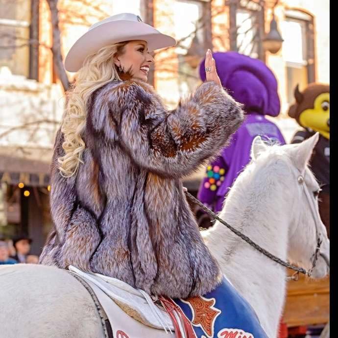 A woman in a fur coat is riding a white horse