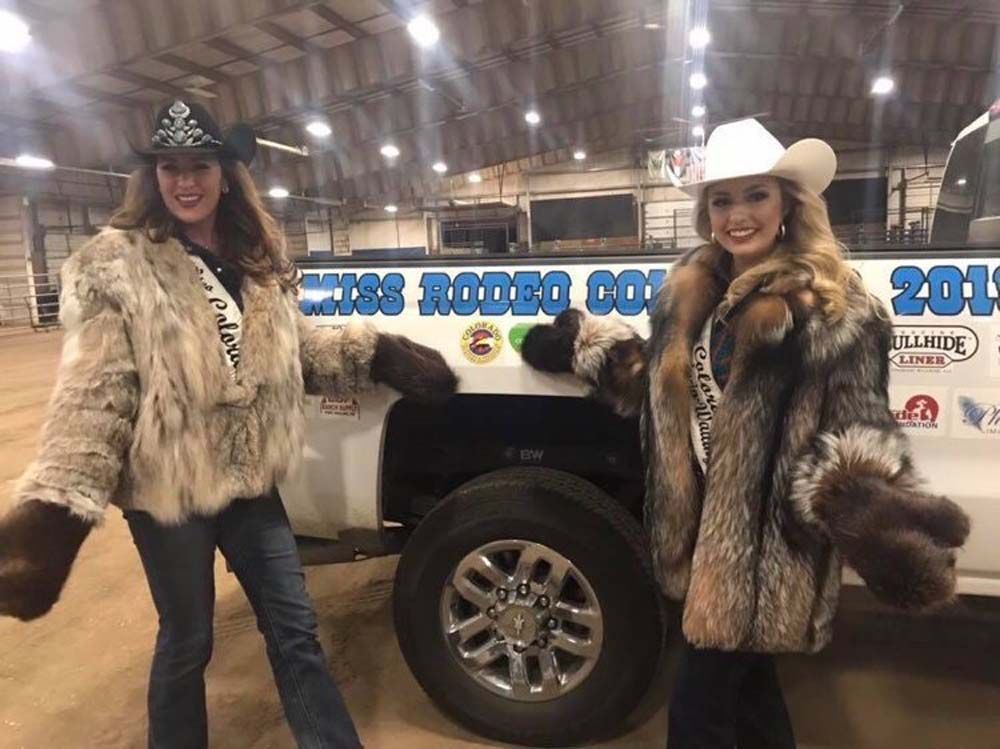 Two women in fur coats and cowboy hats are standing next to a truck.