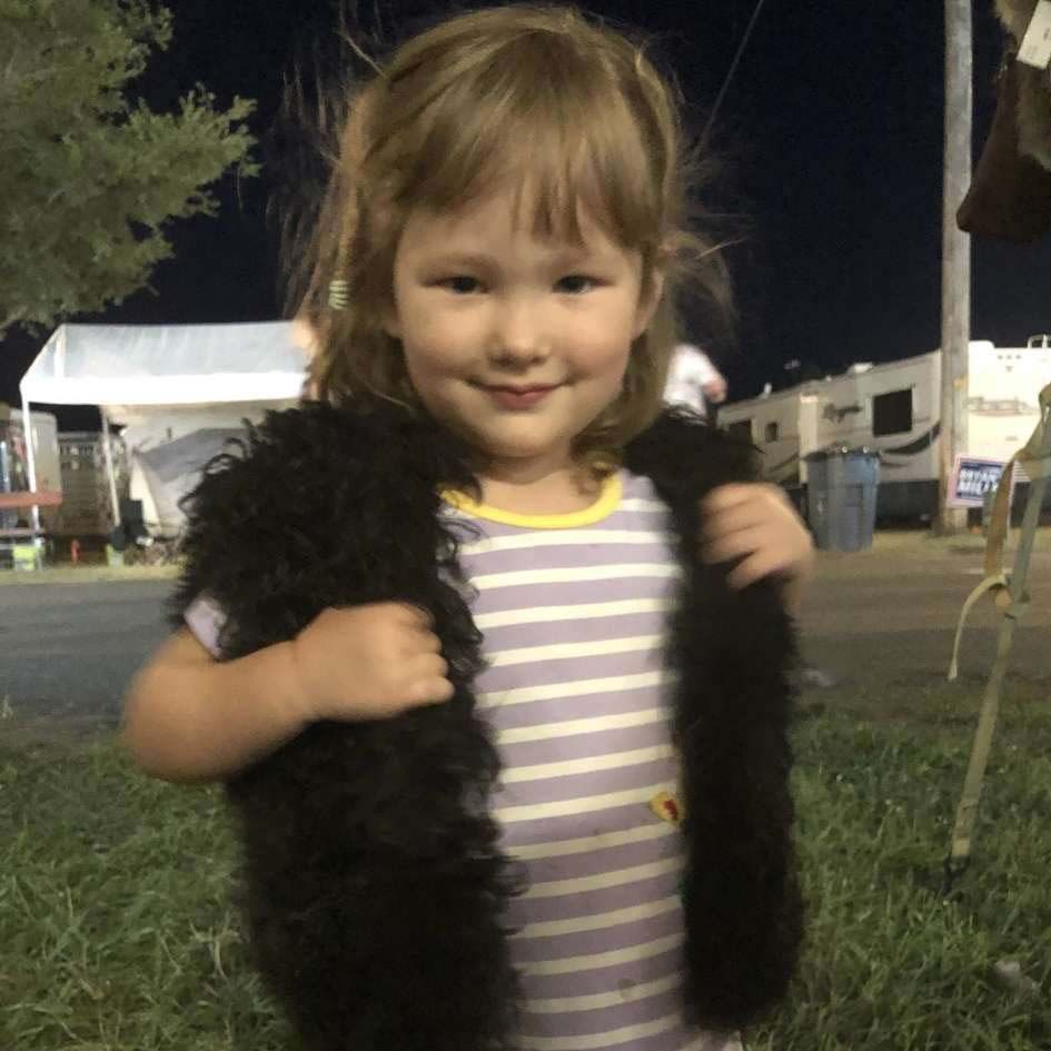 A little girl wearing a fur vest and a striped shirt