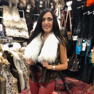 A woman wearing a fur vest and red pants is standing in a store.