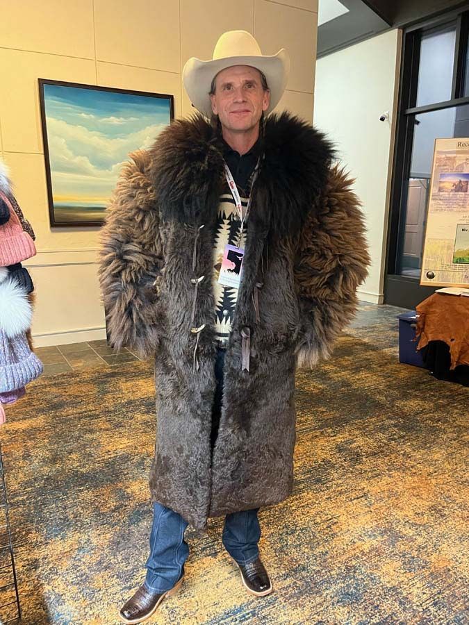 A man wearing a cowboy hat and a fur coat is standing in a room.