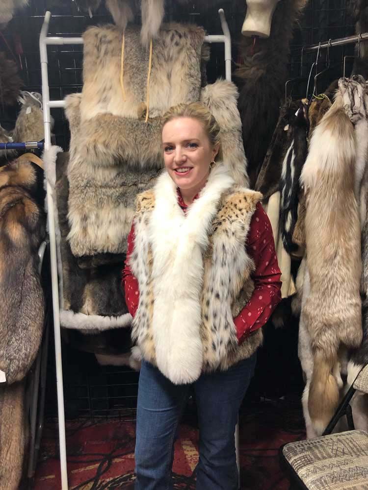 A woman wearing a fur vest is standing in front of a rack of furs.