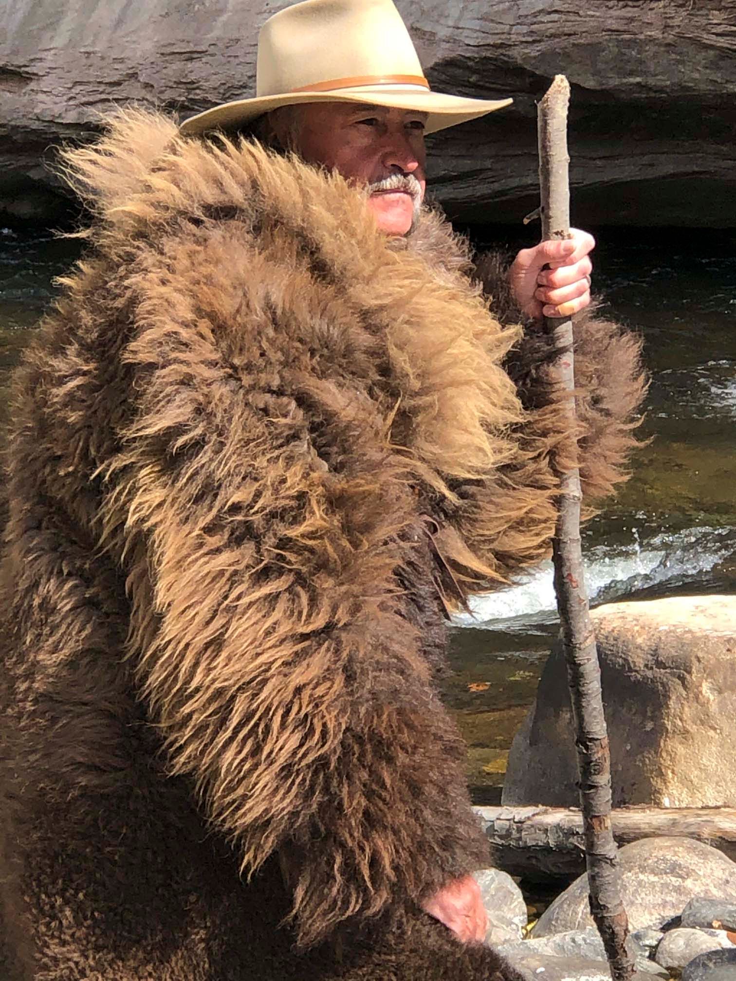 A man in a fur coat and hat is holding a stick.