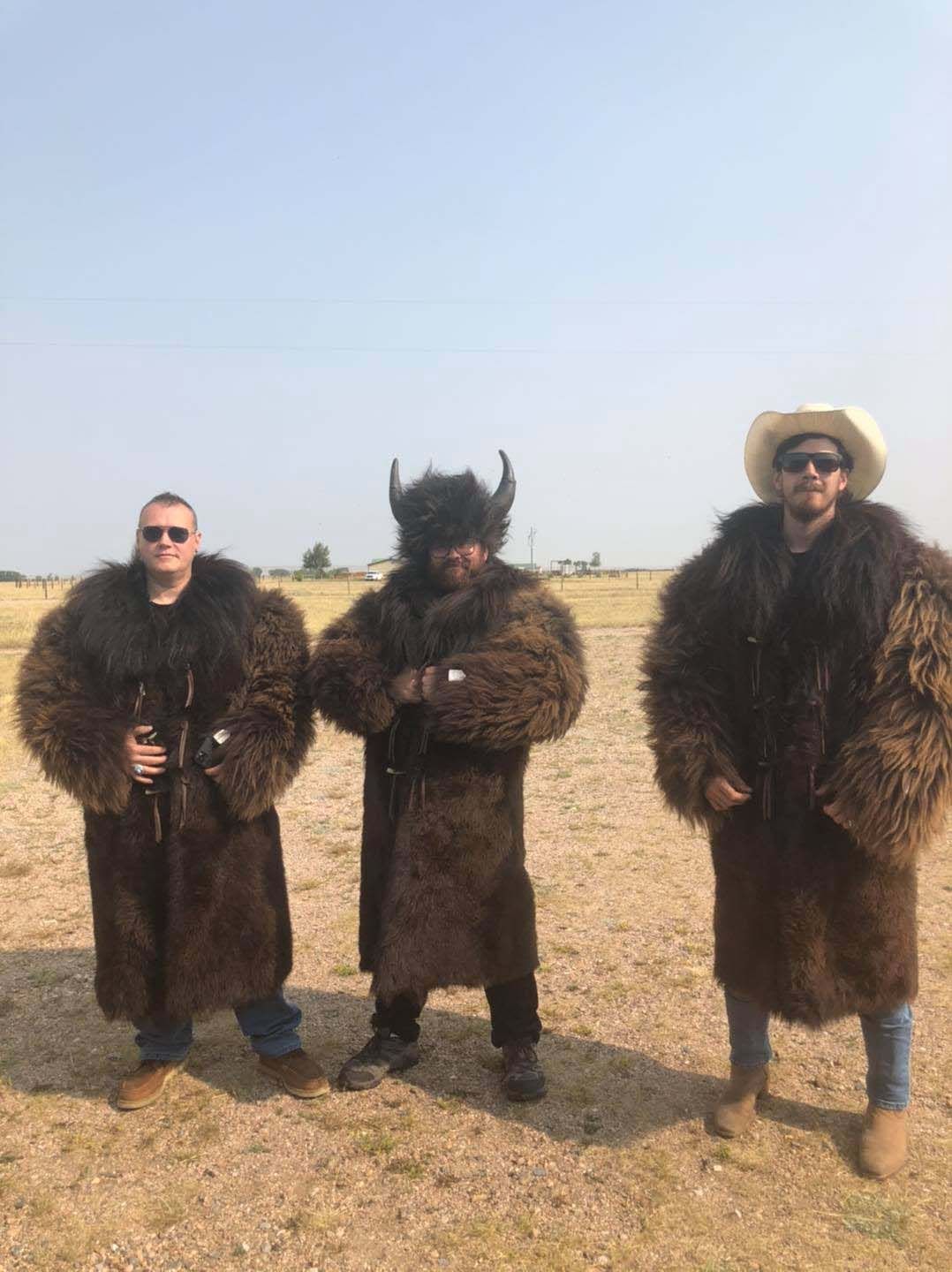 Three men in fur coats and hats are standing in a field.